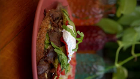 disparo vertical en cámara lenta de un sándwich de carne de res cubierto de rúcula mozzarella queso pepinillos pepino y tomate servido con ensalada