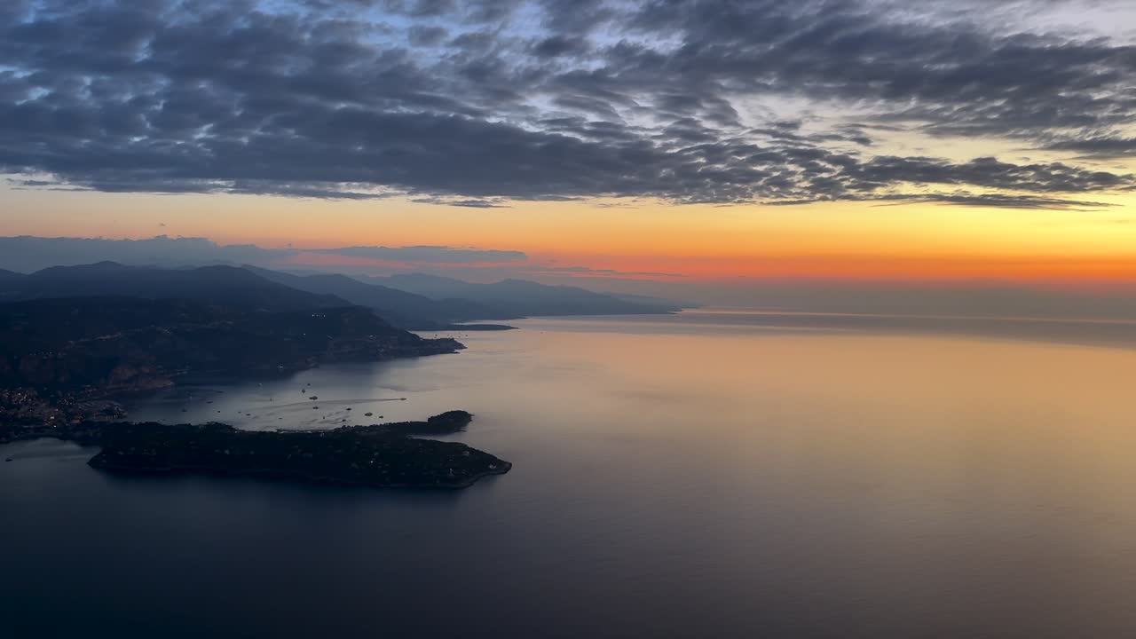An aerial view of the French Riviera coast near Nice city at sunrise, wiith an orange color sky and few cllouds above. Shot taken from a jet cockpit