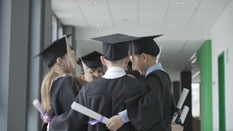 group of happy multiracial preschool students in mortarboard and gown. they are hugging and jumping.