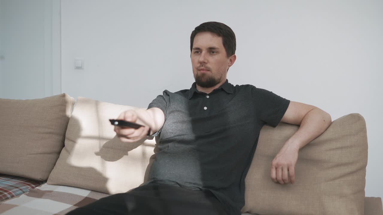 young man watching television and flipping channels on TV sitting on sofa