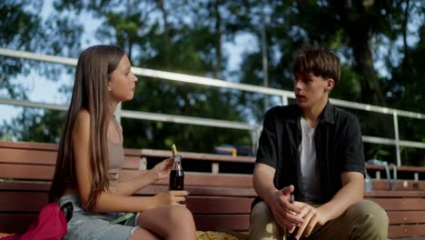 teenage girl and boy sitting on a bench talking and eating pizza