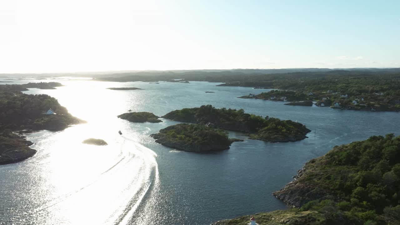 A boat navigates calmly through sparkling blue waters in a remote archipelago. The sun sets, casting golden reflections on the waves while gentle waves lap against rugged shores