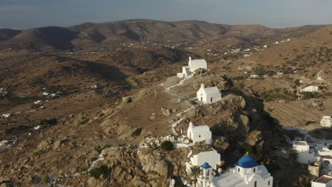 Drohne-Luftaufnahmen-Der-Stadt-Chora-Mit-Kirchen-Auf-Dem-Hügel-Bei-Sonnenuntergang,-Weißes-Gebäude-In-Ios-Griechenland