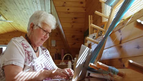 side view of old caucasian senior woman working on laptop and sitting at desk in workshop 4k