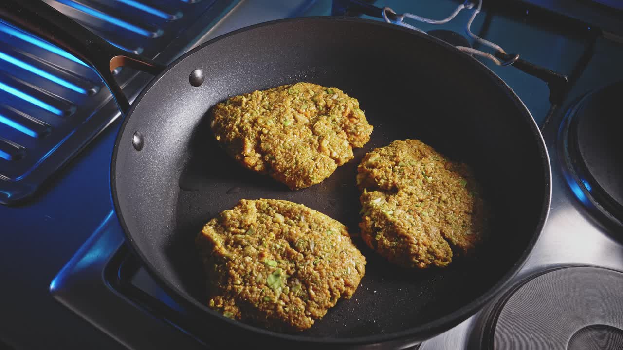 Man flipping veggie patties and covering the non-stick frying pan with tempered glass, close-up shot