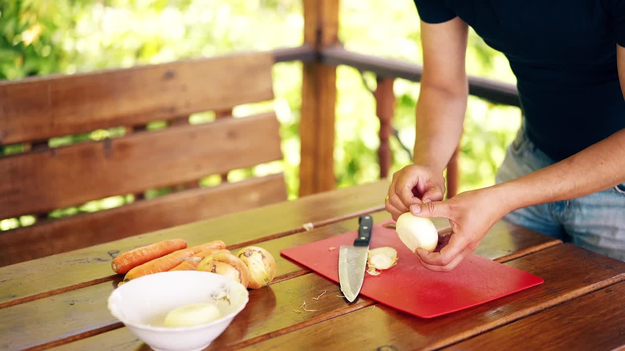 Primer plano de un hombre viajero de pie en una casa de verano cocinando pilaf para un pícnic. Corta cebolla.