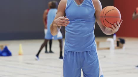 Portrait-of-happy-of-caucasian-male-basketball-player-holding-ball-at-indoor-court,-slow-motion