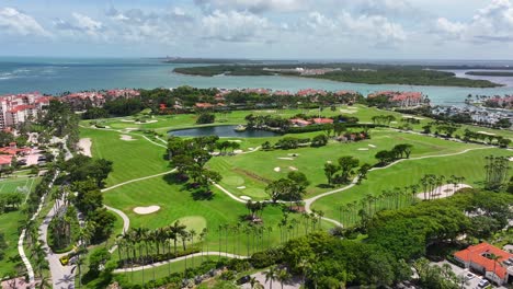 a sprawling golf course on fisher island is surrounded by palm trees and waterfront views of biscayne bay