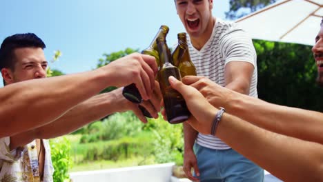 group of happy friends toasting beer bottles at outdoors barbecue party