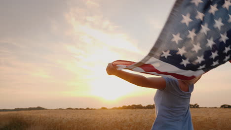 Frau-Mit-USA-Flagge-Läuft-In-Der-Sonne-Auf-Einem-Weizenfeld