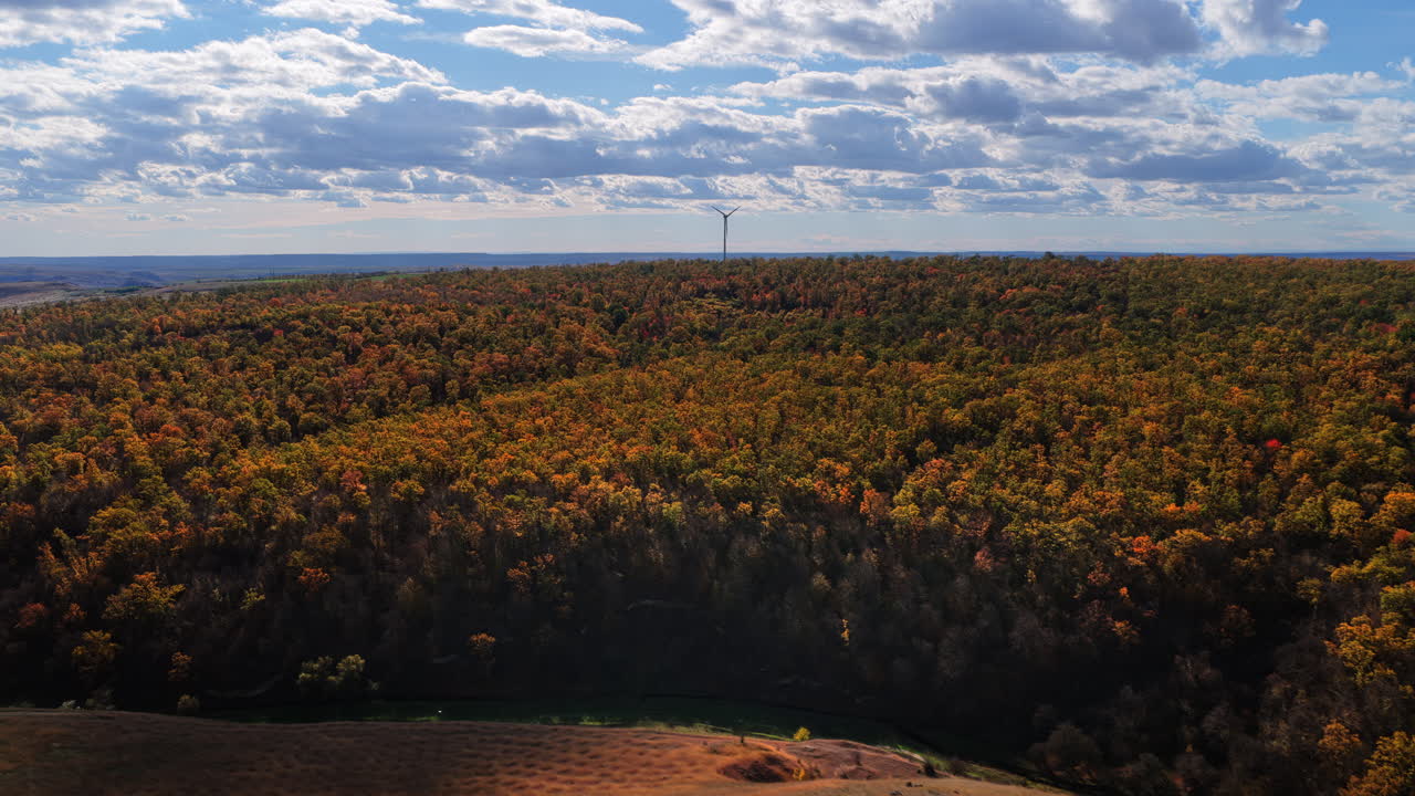 Aerial drone view of a wind turbine above colorful autumn forests and rolling hills in Moldova