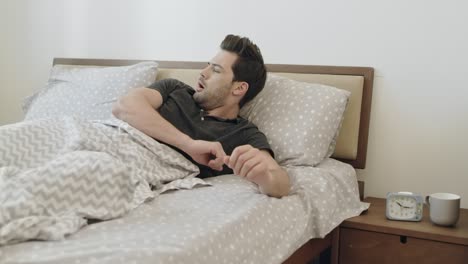 lethargic man waking up in morning slowly. handsome guy sitting on bed.