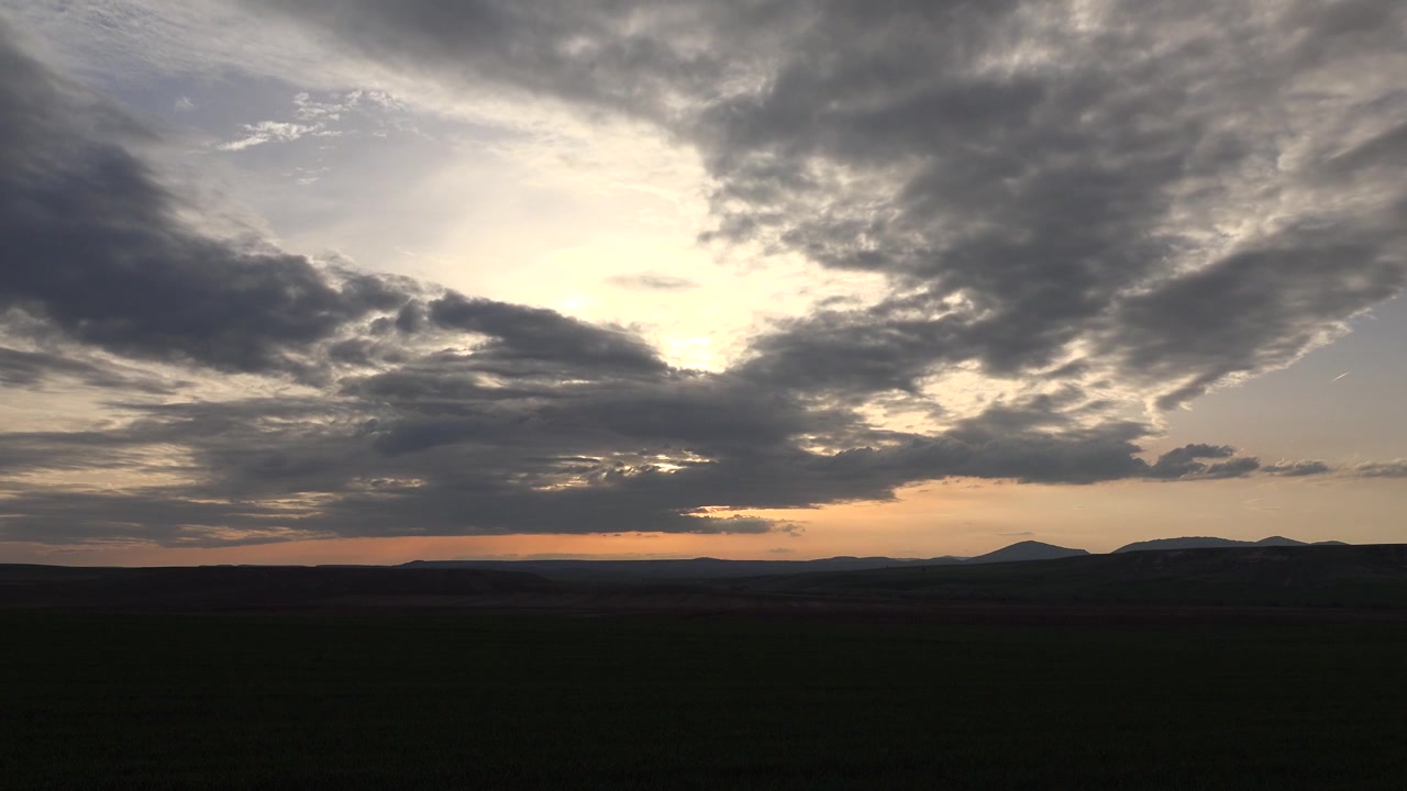 Dramatic Sunset Over Dark Rolling Hills and Cloudy Sky