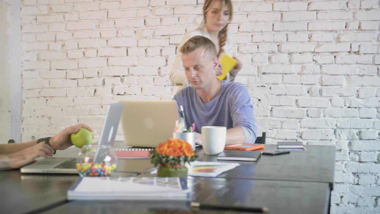 деловые коллеги работают с ноутбуками, бизнес-партнерка подходит к ним и обсуждает что-то за столом в офисе.