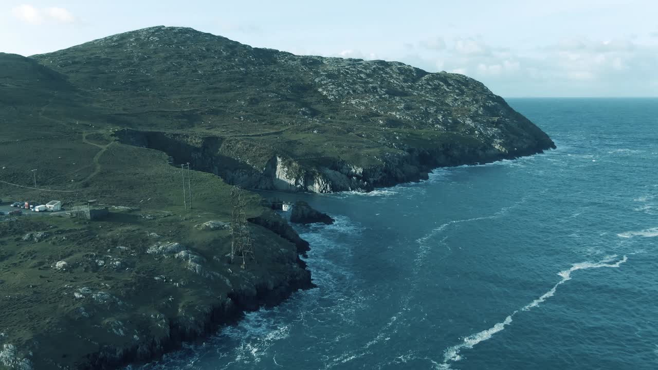 Aerial pedestal up showing cable car traveling over waves crashing into rocky shoreline reveling rocky irish island and coastline