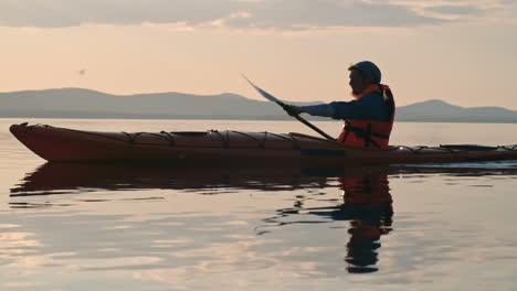 vista lateral de un hombre con gorra y chaleco salvavidas remando en una canoa en el lago al atardecer 1