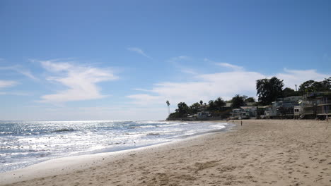 Walking-on-the-sand-at-Miramar-beach-with-ocean-waves-crashing-and-expensive-beach-houses-on-the-shore-lining-the-coast-of-Montecito,-California-SLOW-MOTION