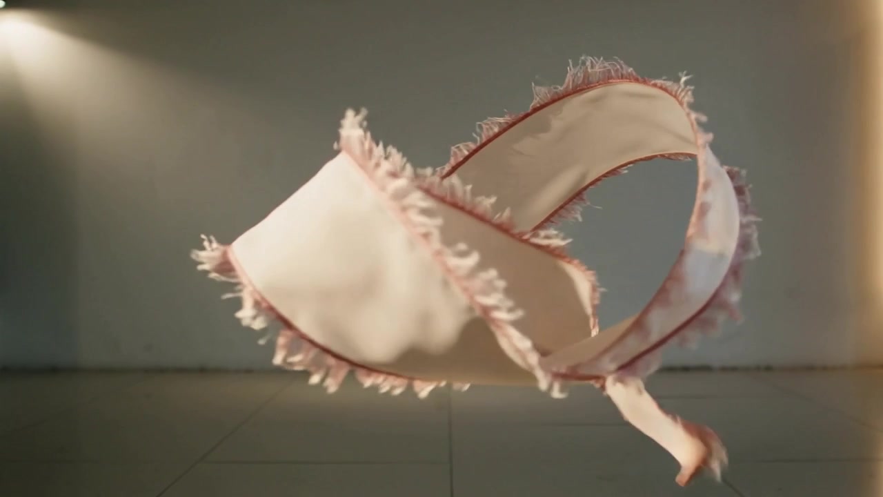 Entering lower-left, pale-pink frayed ribbon floating, spiraling and unfurling across studio floor