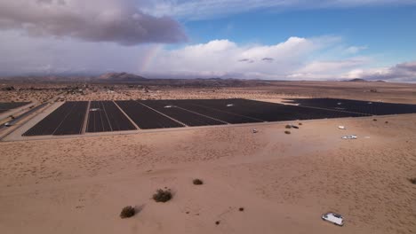 Aerial-Drone-Footage-of-Solar-Panel-Field-in-Joshua-Tree-National-Park-on-a-Sunny-Day-with-rainbow-in-the-background,-wide-horizontal-pan