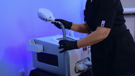 beauty specialist in black uniform takes the laser for hair removal. woman turns the keys in machine to switch the apparatus.