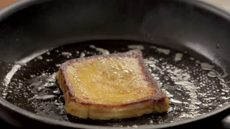 man's hand turns bread in pan with butter