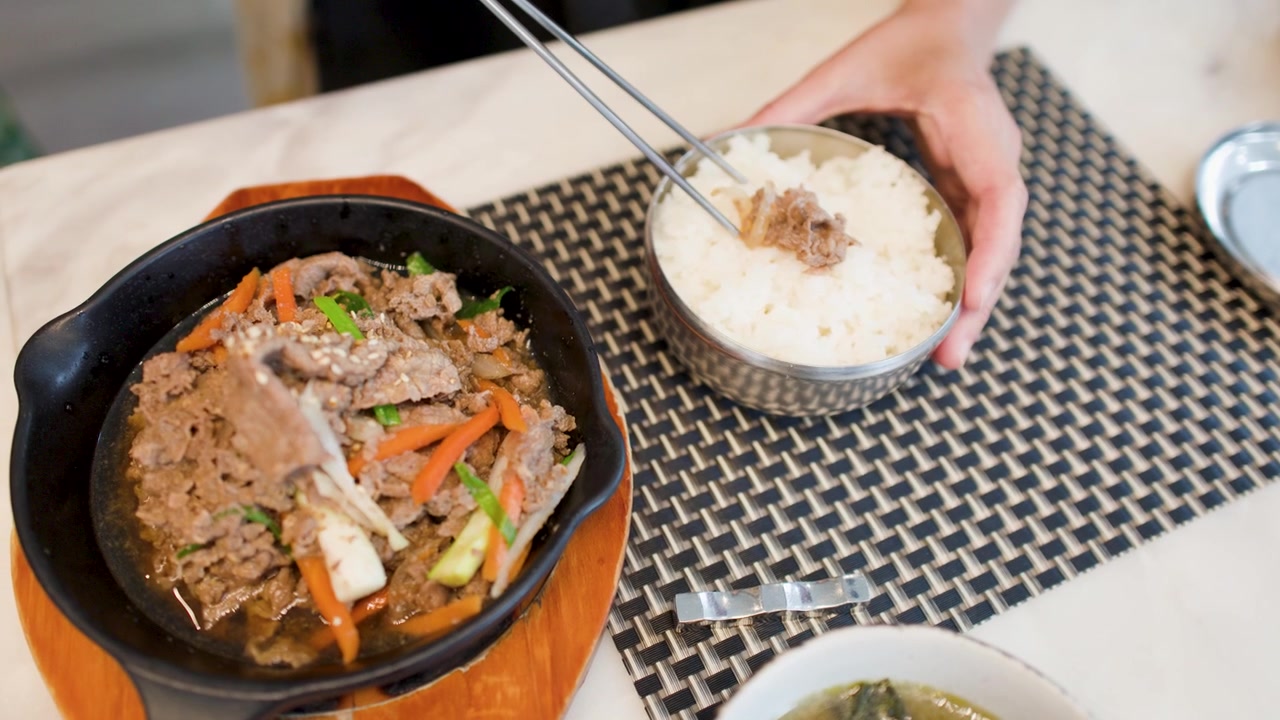 คนกำลังกินบุลโกกิเนื้อเกาหลีกับข้าวสวยโดยใช้ตะเกียบโลหะแบบดั้งเดิม มุมมองจากด้านบน