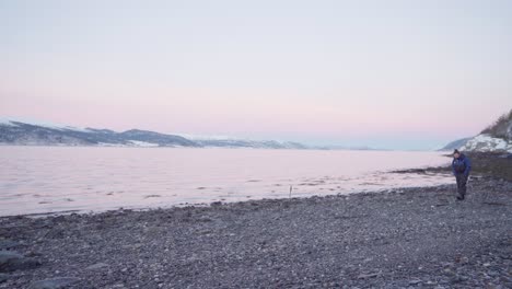 lone man with his pet dog walks along the stony shoreline of a peaceful ocean