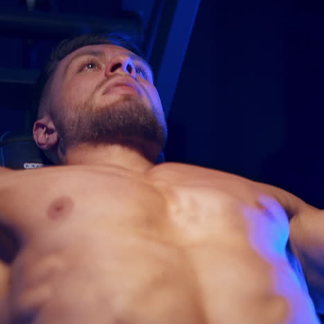 bodybuilder doing workout in the gym. strong man with naked torso training his muscles on a simulator. close-up. blue filter.