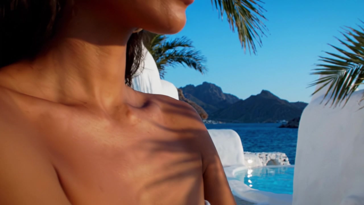 Un primo piano mozzafiato di una mano che indossa un braccialetto vivace su uno sfondo panoramico di acque blu e montagne, catturando eleganza e bellezza naturale.