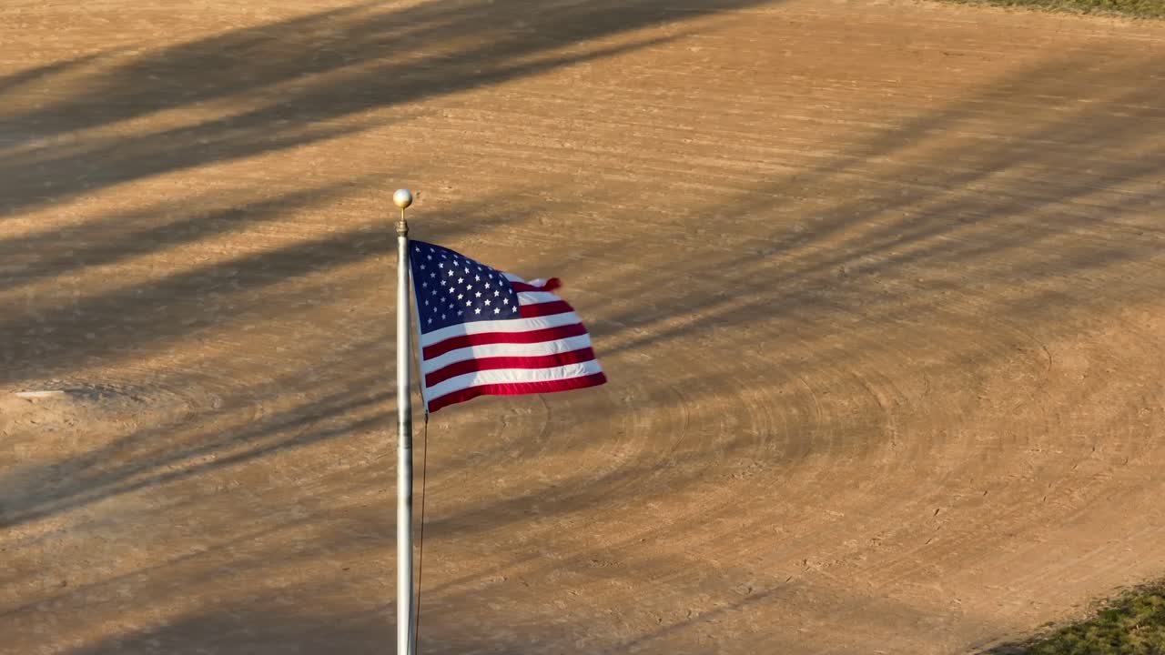 bandera estadounidense ondeando con el campo de béisbol tierra infield en el fondo