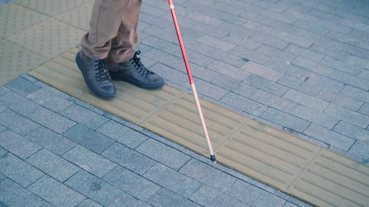 hombre con discapacidad visual está caminando en una baldosa de advertencia táctil con la ayuda de su bastón. superficie de advertencia detectable para los discapacitados visuales al aire libre en la ciudad.