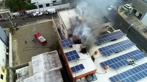 Aerial-view-of-smoke-rising-from-a-building-fire,-with-solar-power-panels-on-the-roof,-in-Manila-city,-Philippines---pull-back,-drone-shot