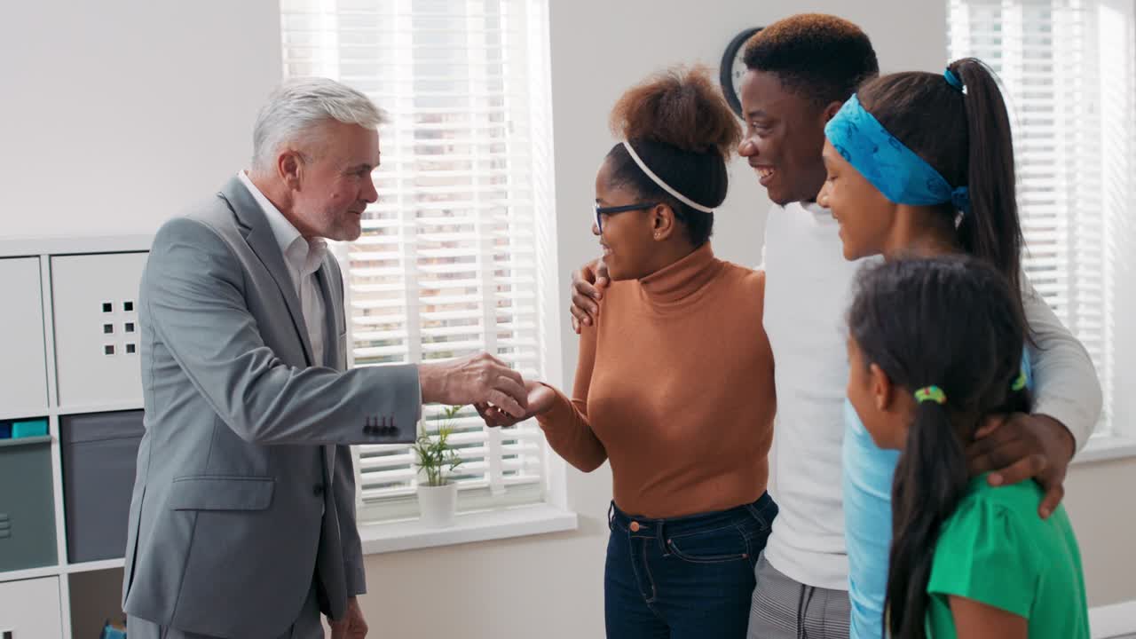 un anciano de cabello gris, un agente de bienes raíces vende un apartamento a una pareja joven con hijos, le da a la mujer las llaves explicando los detalles, la familia se abraza con felicidad