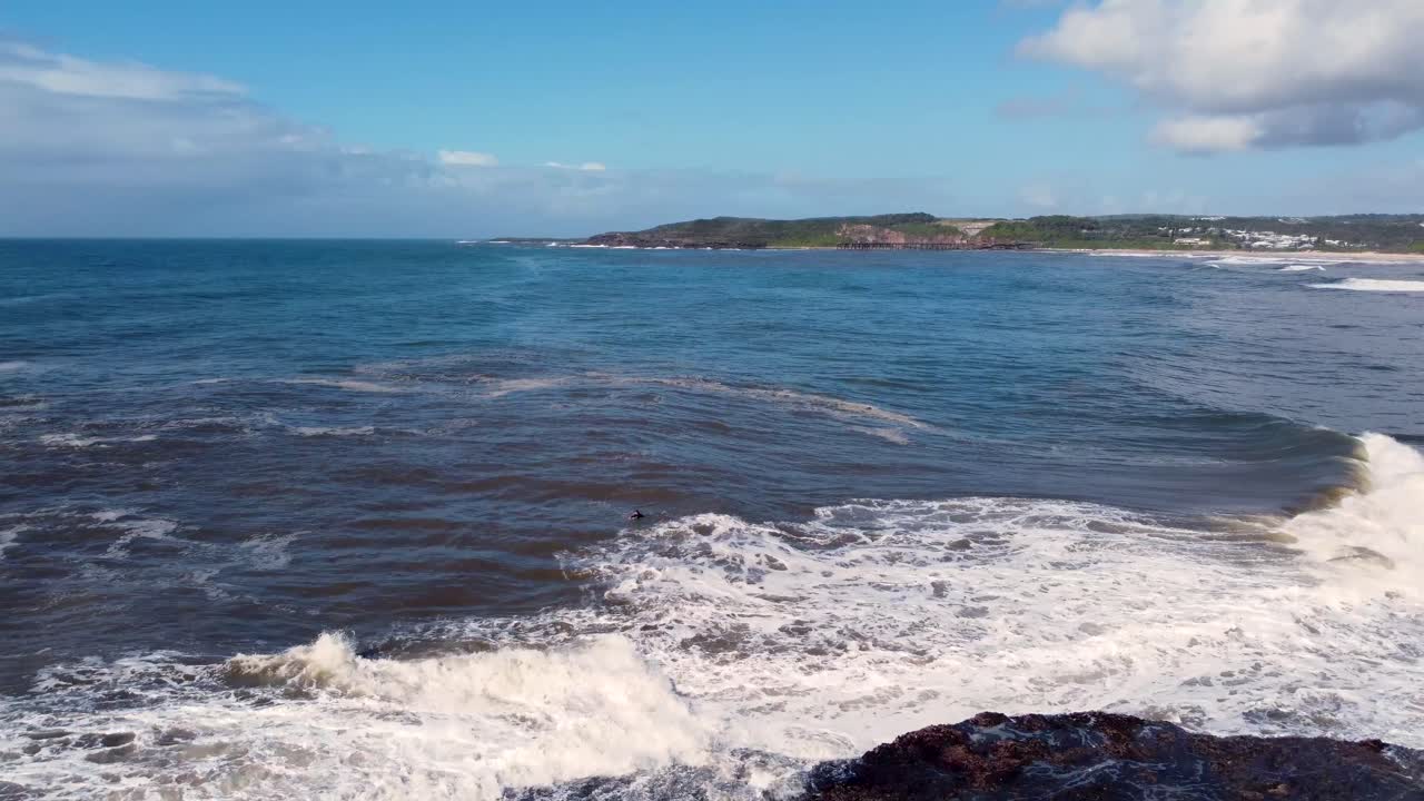 panorámica aérea de drones toma escénica de bodyboarder esperando en la playa de olas de arrecifes rocosos océano pacífico newcastle nueva gales del sur australia 4k