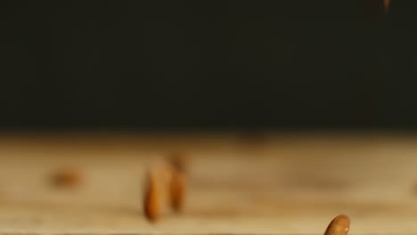 close up shot of almond nuts dropping onto wooden surface against black studio background shot in slow motion 1