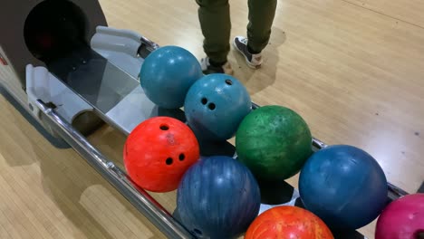 un joven toma una pelota de bolos amarilla de un rollo