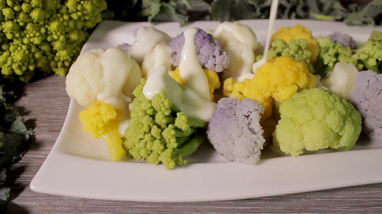 Pouring bechamel on colorful broccoli cauliflowers plate