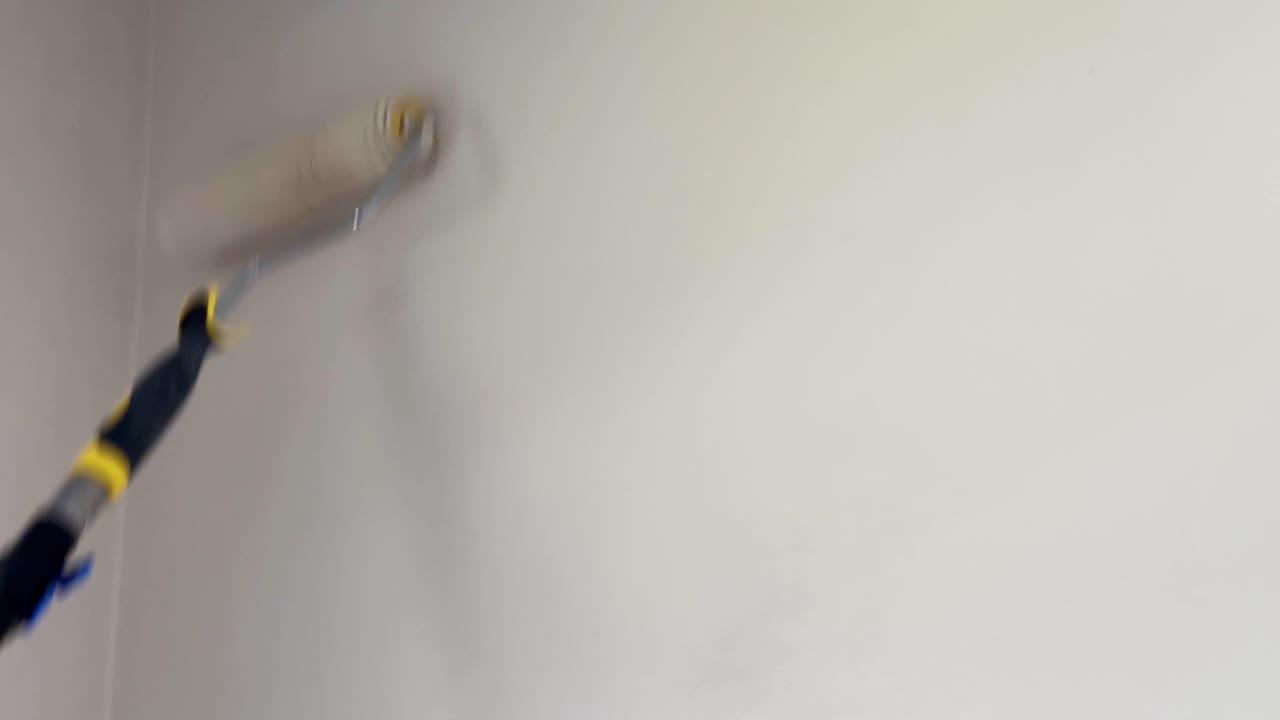 rodillo de pintura que aplica pintura de color crema marfil a las paredes de una habitación luminosa