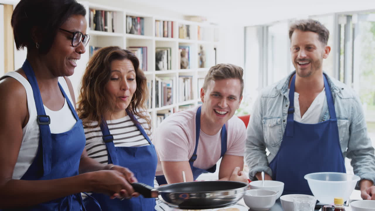 성인 학생 들 이 지켜보고 있는 요리 수업 에서 여자 교사 가 플래트브레드 팬 을 뒤집고 있다