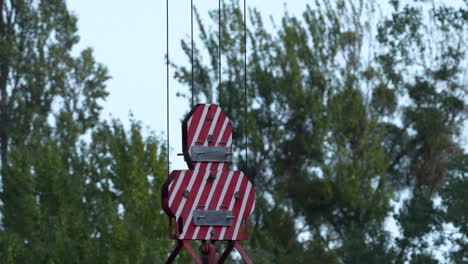 pinzas de construcción rojas y blancas suspendidas por cables contra un telón de fondo de árboles, indicando trabajos de construcción o reparación