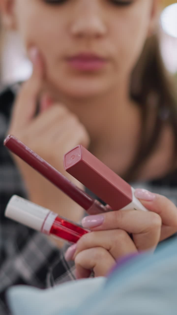 Woman choosing lip products, She evaluates lip products with careful consideration in store setting, Focused young woman compares various lip enhancement products before purchasing at retail shop