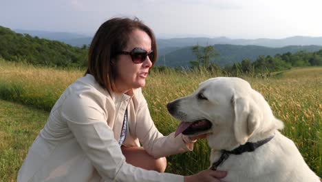 medium shot of woman playing with white lab dog with mountain backdrop