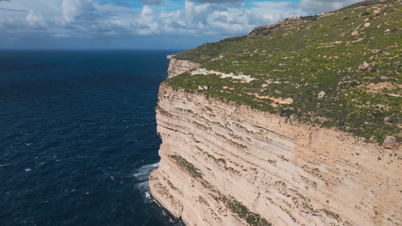 Cinematic drone flight over the rugged edge of Dingli Cliffs in Malta, showing contrast between green plateau and deep blue mediterranean sea