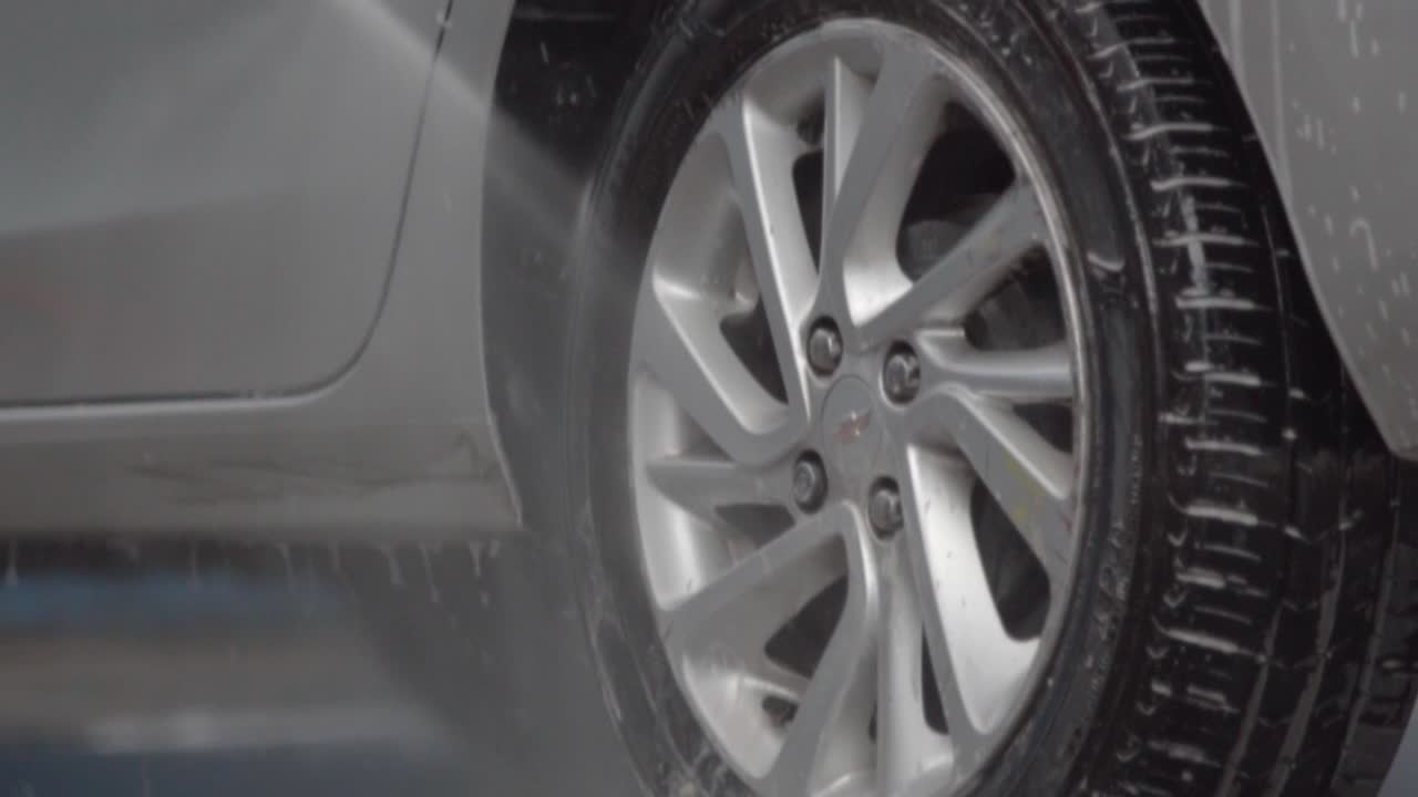 Close up of washing a car tire with foam and pressurized water. Car wash.