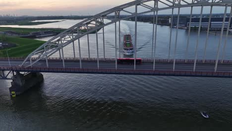 Coches-Circulando-A-Través-Del-Puente-De-Arco-Con-Un-Crucero-Por-El-Río-Navegando-En-El-Río-Noord-Al-Atardecer-En-Hendrik-ido-ambacht,-Países-Bajos