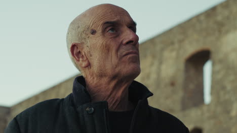 elderly bald tourist man takes off his woolen hat and looks at the building