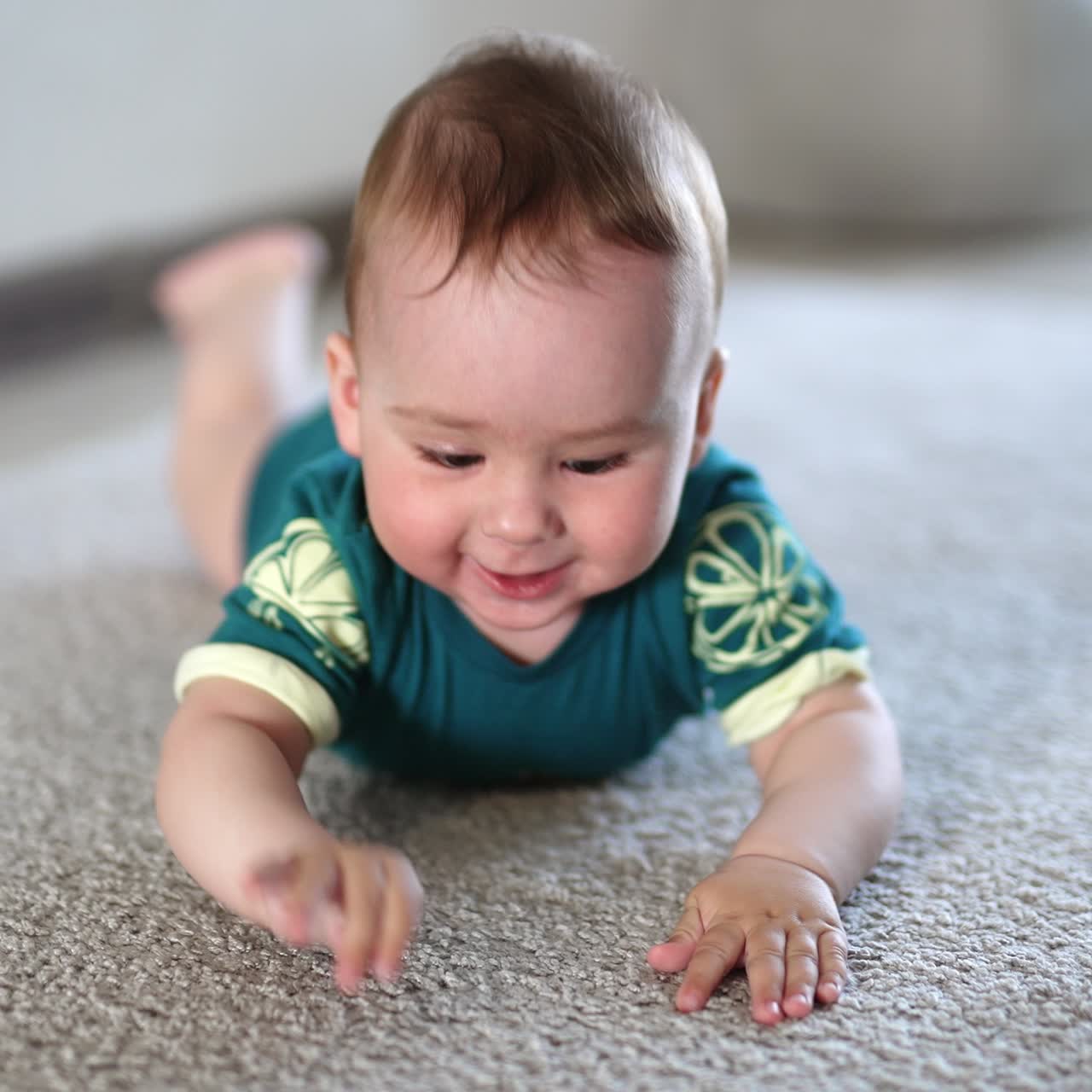 Cheerful happy Caucasian baby boy lies on belly smiling. Adorable child banging his limbs over the floor actively