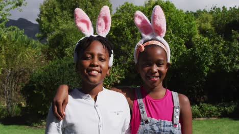 smiling african american brother and sister wearing easter bunny ears embracing in garden
