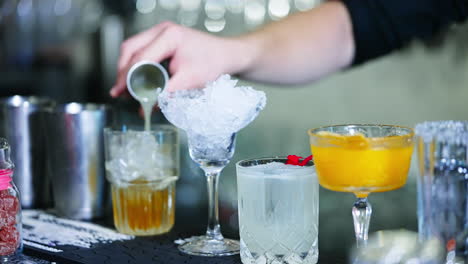 preparation of cocktails in the bar. bartender in black shirt fills the beaker with beverage and adds it to the glass.