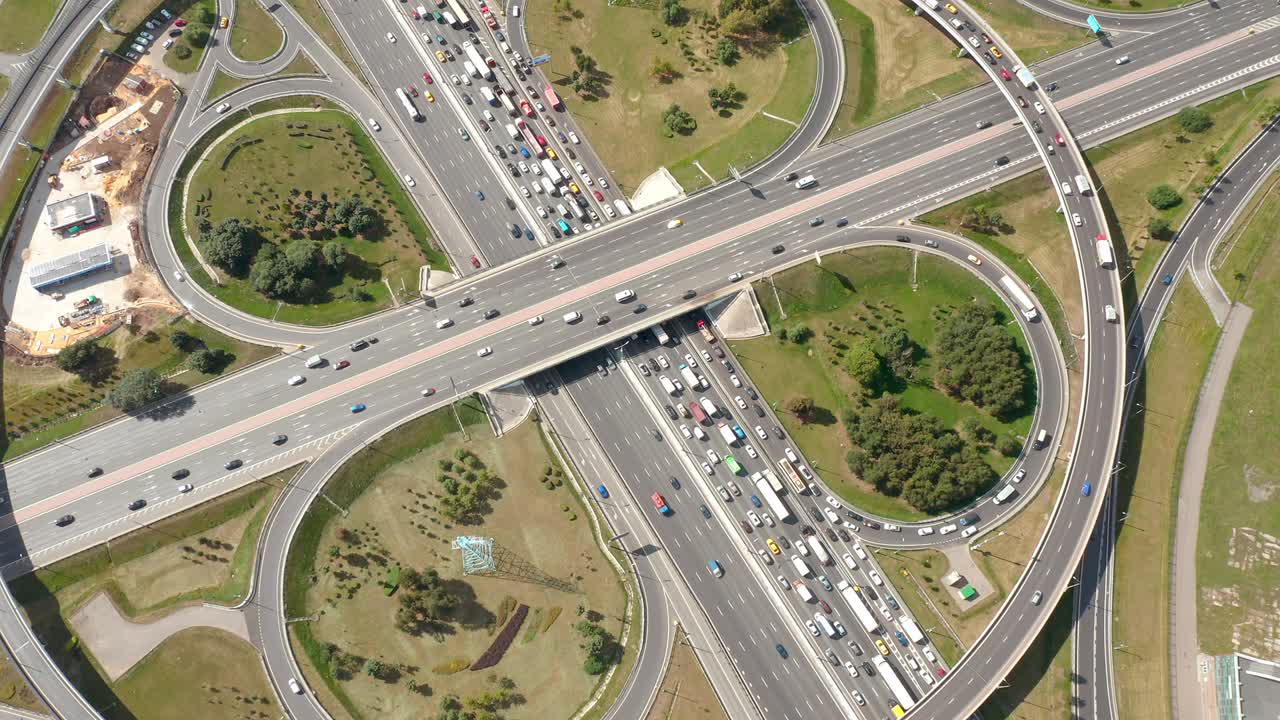 una gran intersección con salidas de trébol y tráfico pesado. vista aérea de arriba hacia abajo desde un avión no tripulado. rutina de tráfico típica conceptual. luz solar. áreas de plantación verdes a su alrededor. la cámara se mueve hacia adelante bajo la autopista.